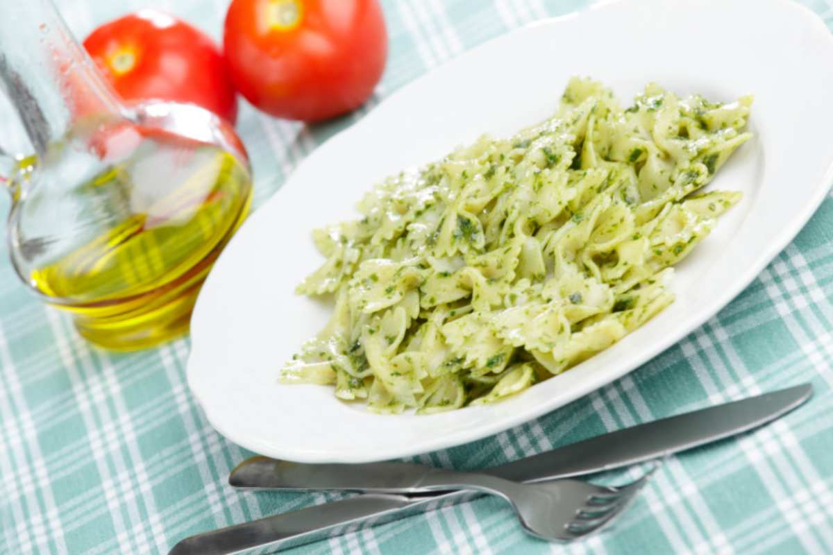 farfalle al pesto con accanto una bottiglia di olio e dei pomodori