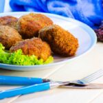 polpette fritte su un piatto con accanto dell'insalata e vicino delle posate