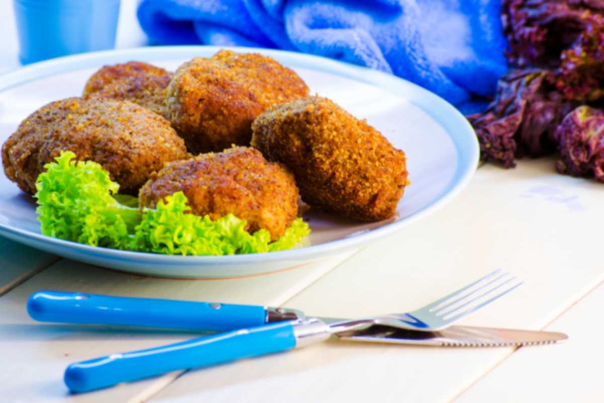 polpette fritte su un piatto con accanto dell'insalata e vicino delle posate