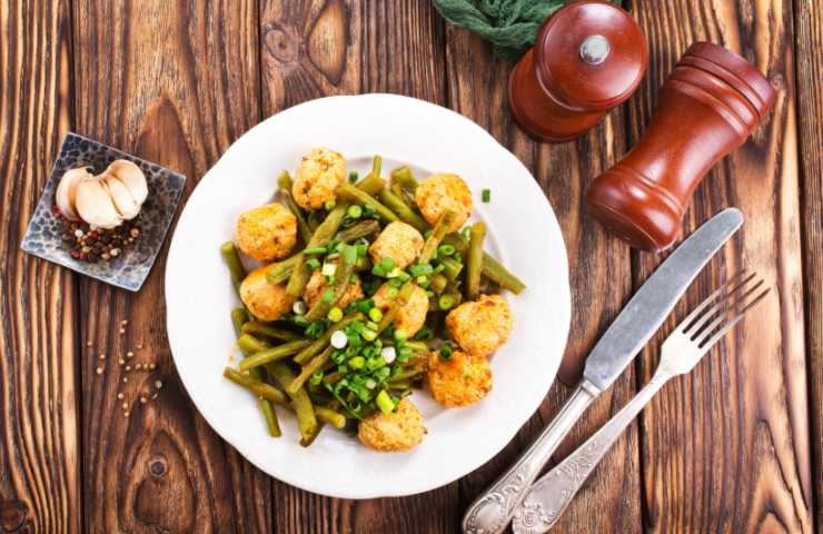 polpette in un piatto con dei fagiolini e vicino delle posate e dell'aglio