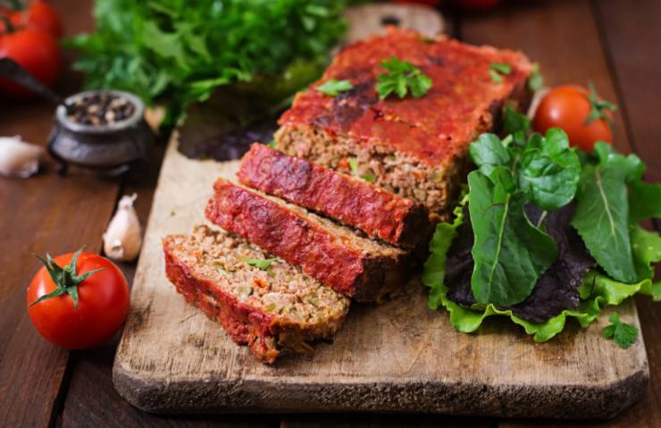 polpettone sopra ad un tagliere con accanto verdura, pomodori e aglio