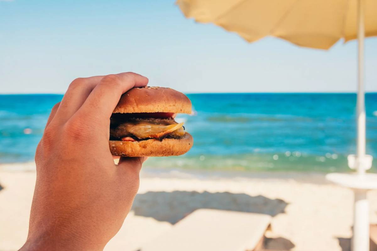 Persona che tiene un panino in spiaggia