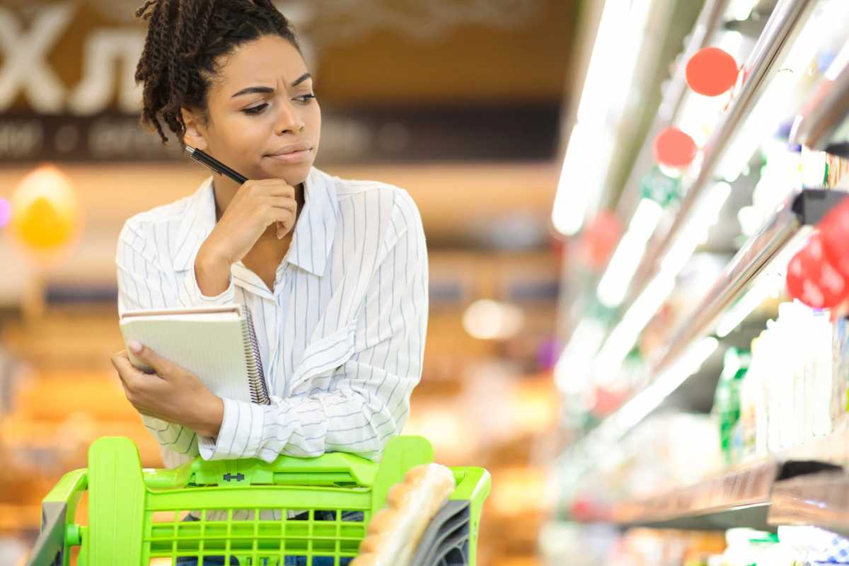 Donna in un supermercato con carrello che guarda scaffale pensierosa