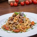 Piatto di spaghetti conditi con pomodorini, tonno, acciughe ed erbe aromatiche