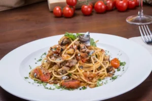Piatto di spaghetti conditi con pomodorini, tonno, acciughe ed erbe aromatiche