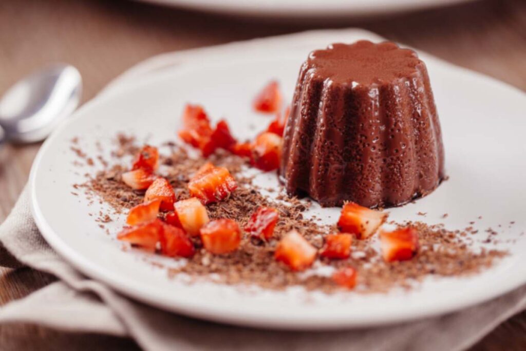 budino al cioccolato su un piatto con intorno del cacao e delle fragole