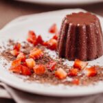budino al cioccolato su un piatto con intorno del cacao e delle fragole