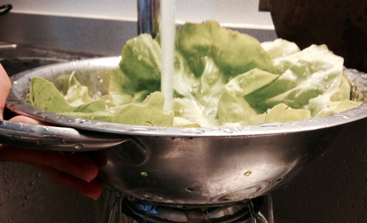 Insalata in uno scolapasta con acqua che cade dal rubinetto