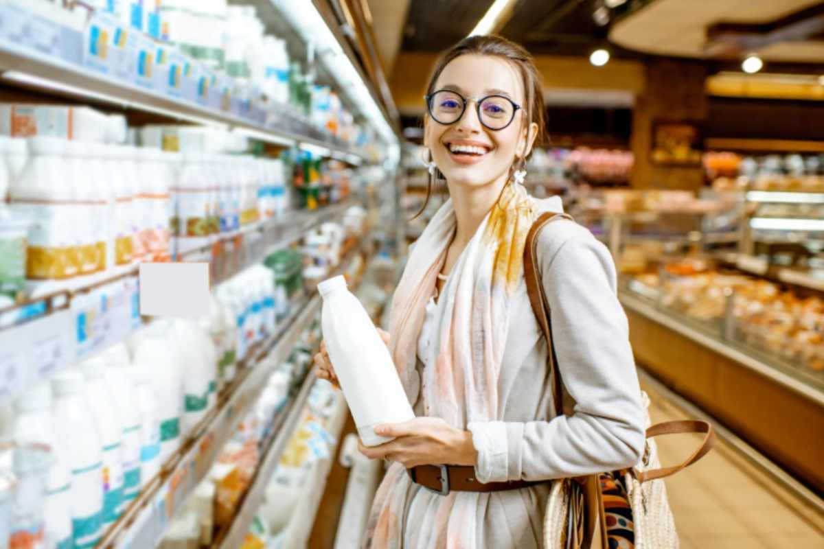donna che sorride al supermercato con in mano una bottiglia di latte