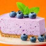 etta di torta ai mirtilli sopra ad un piatto con sopra mirtilli e qualche foglia di menta