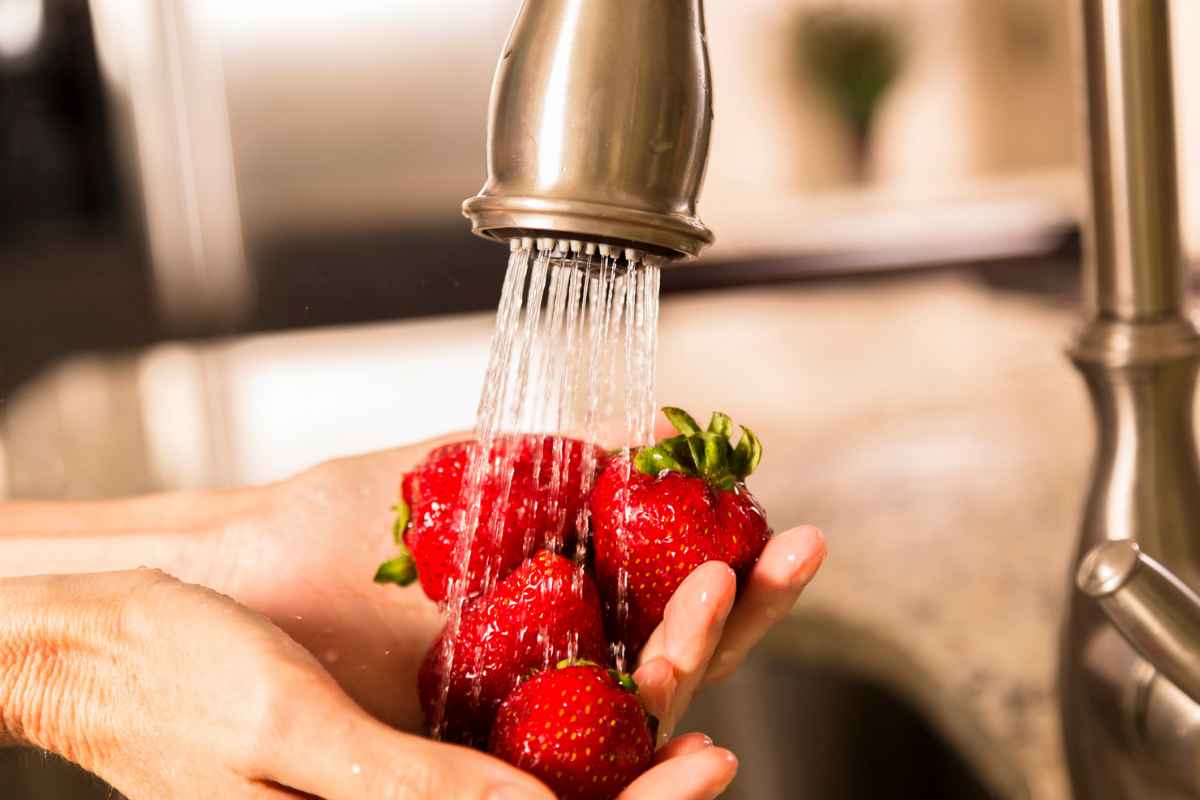 Persona che lava le fragole sotto l'acqua del rubinetto