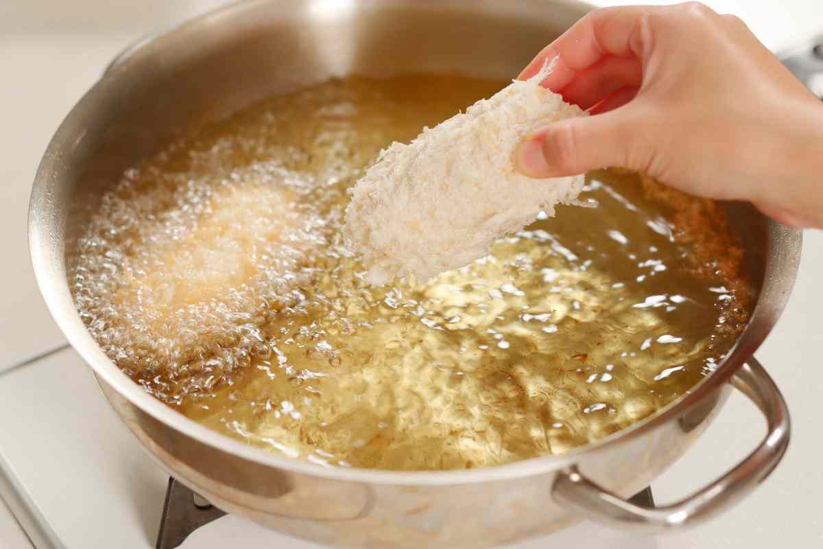 Persona che frigge pollo in una pentola con olio