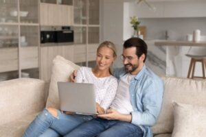 uomo e donna seduti sul divano che sorridono mentre guardano qualcosa sul computer