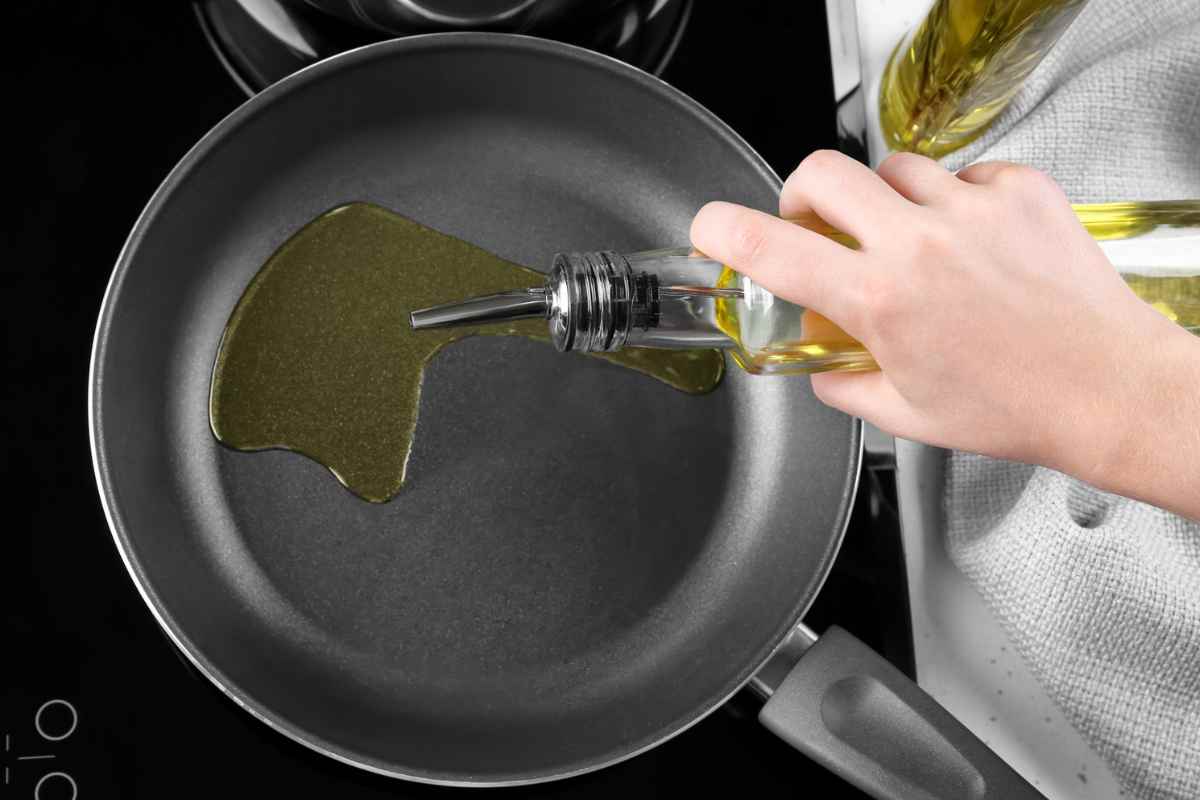 Persona che versa olio di oliva in una padella