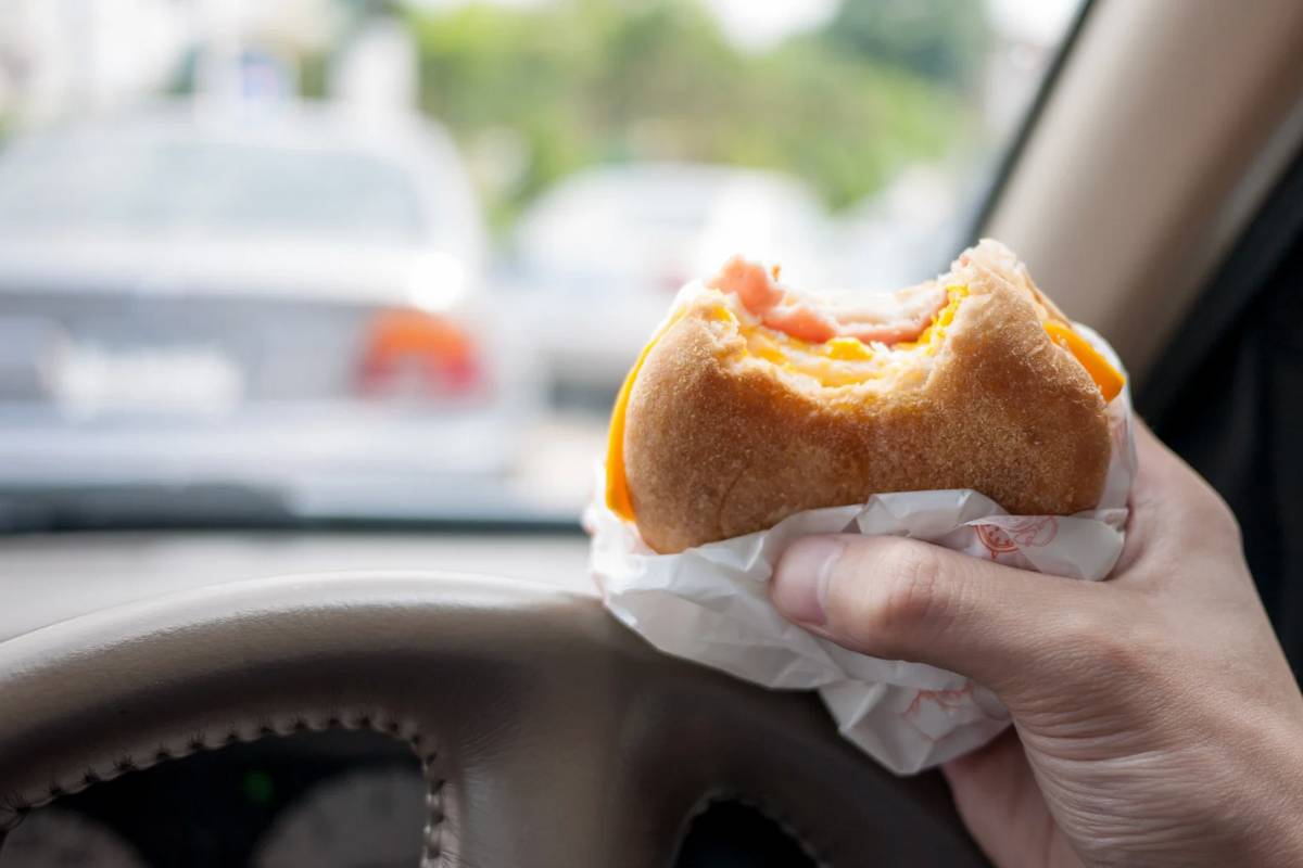 Persona che tiene in mano un panino in macchina