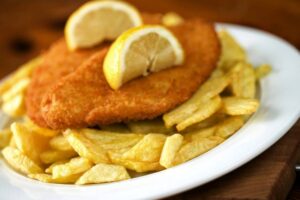 cotolette in un piatto circondate da patatine fritte con sopra due spicchi di limone