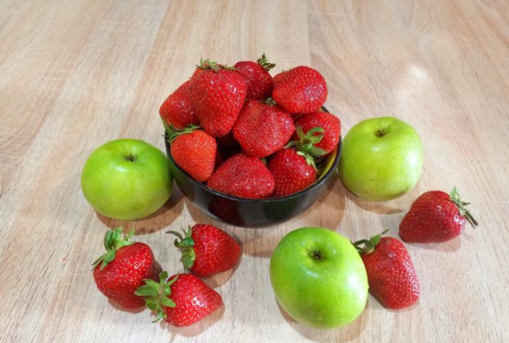 mele e fragole sparse in una ciotola e su un tavolo