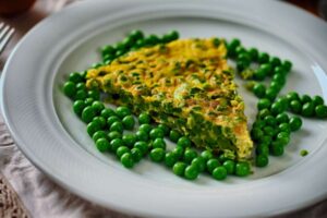 fetta di farifrittata di zucchine e piselli con intorno dei piselli