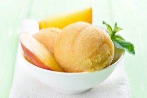 gelato alla pesca dentro ad una coppa con delle fette di pesca e delle foglie di menta