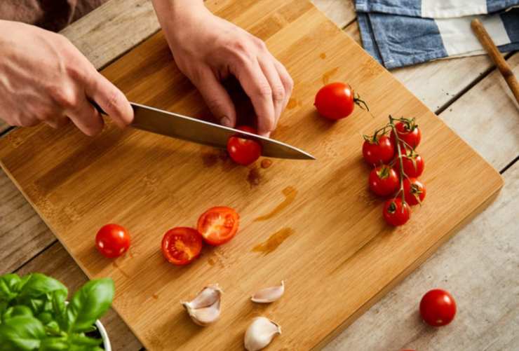 mani che tagliano pomodori su tagliere
