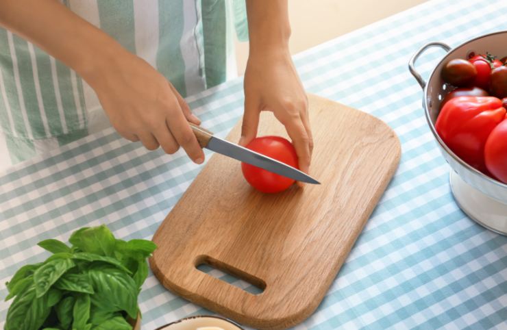 donna che taglia un pomodoro sopra ad un tagliere