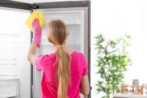 Donna bionda che pulisce l'interno del frigorifero con una spugna gialla