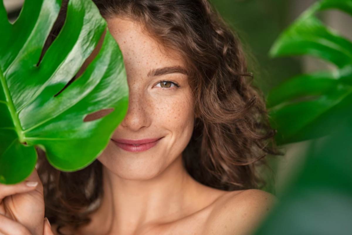 donna che sorride con il viso in mezzo a delle foglie