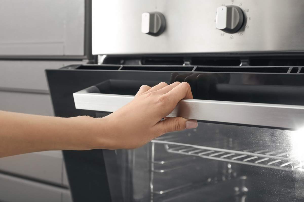 Donna con smalto sulle unghie che apre anta del forno