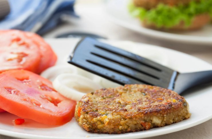 burger vegano in un piatto con accanto dei pomodori