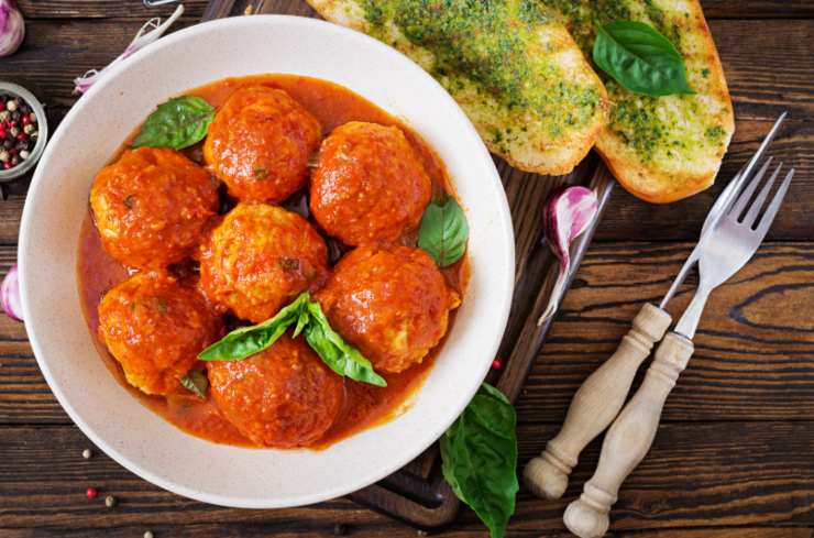 polpette al sugo dentro ad un piatto con sopra delle foglie di basilico