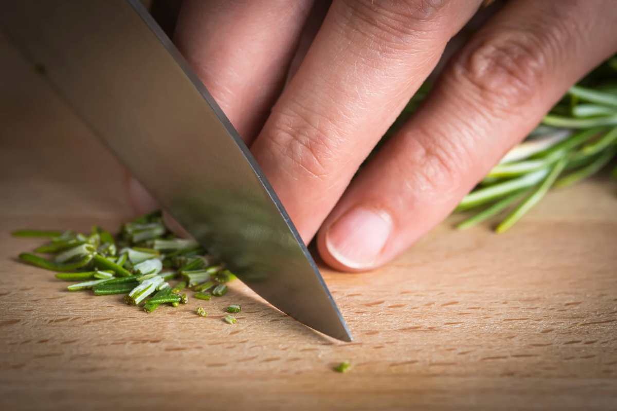 Mani che tagliano rosmarino sul tagliere