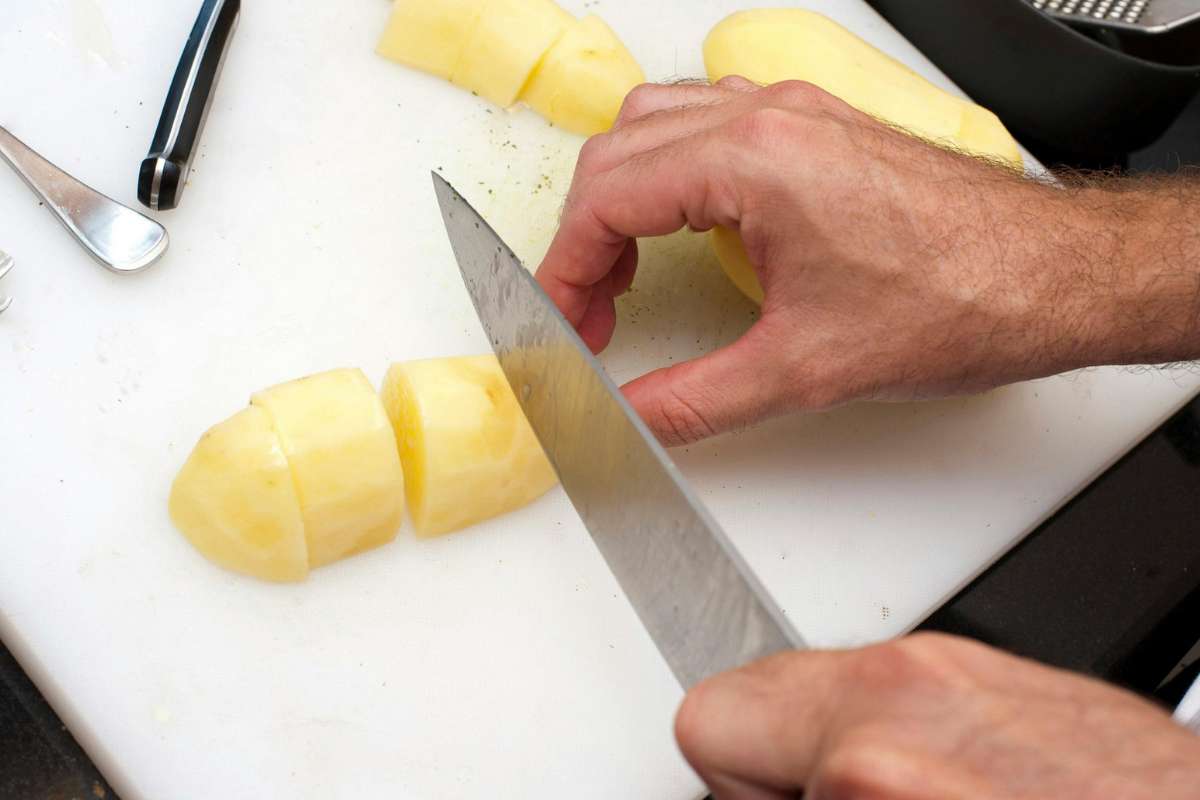 Uomo che taglia patate su un tagliere