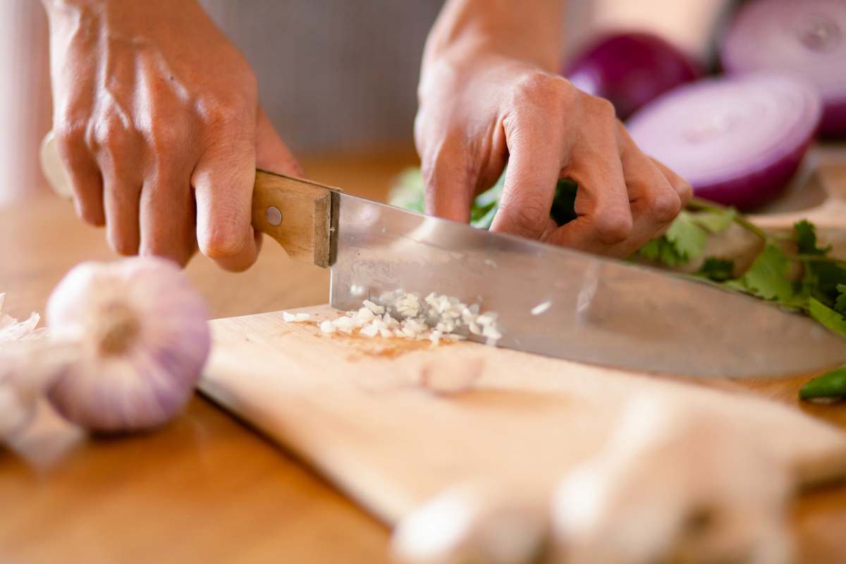 Persona che trita aglio su un tagliere di legno