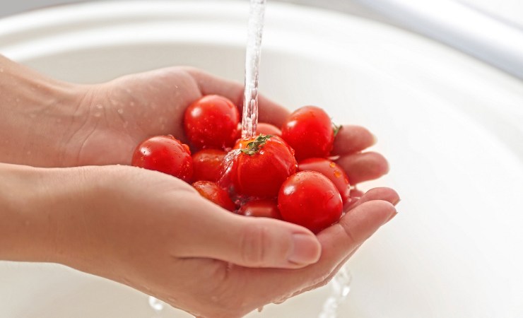 Persona che lava pomodorini sotto l'acqua corrente