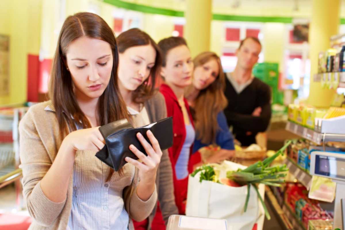 donna che cerca i soldi nel portafoglio alla cassa del supermercato