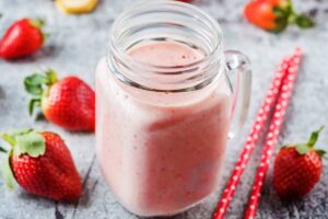 un bicchiere di smoothie con fragole sparse sul tavolo e due cannucce