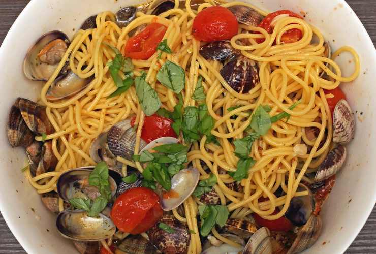 piatto fumante di spaghetti alle vongole con pomodorini e prezzemolo