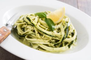 spaghetti di zucchine con sopra uno spicchio di limone e delle foglioline di basilico