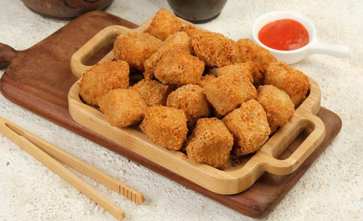 Bocconcini di tofu fritto su un vassoio, con salsa e bacchette accanto