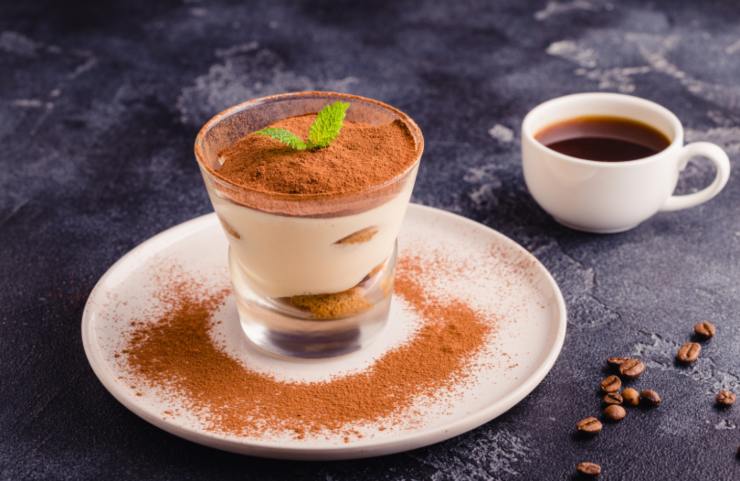 tiramisù dentro ad un bicchiere di vetro e dietro una tazzina di caffè