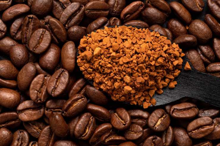 un cucchiaio di caffè in polvere circondato da chicchi di caffè