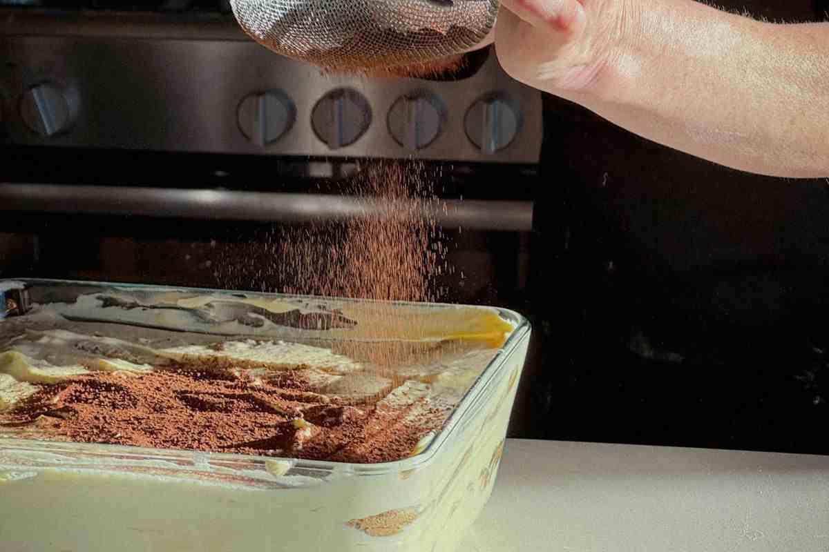 persona spolvera cacao su un tiramisù