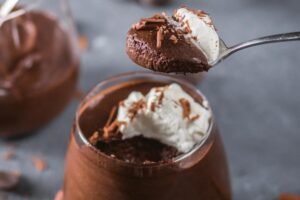 Vasetto con torta al cioccolato e panna e cucchiaino con un boccone abbondante
