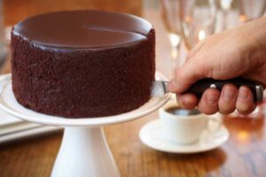 persona che taglia una fetta di torta al cioccolato e dietro una tazzina di caffè