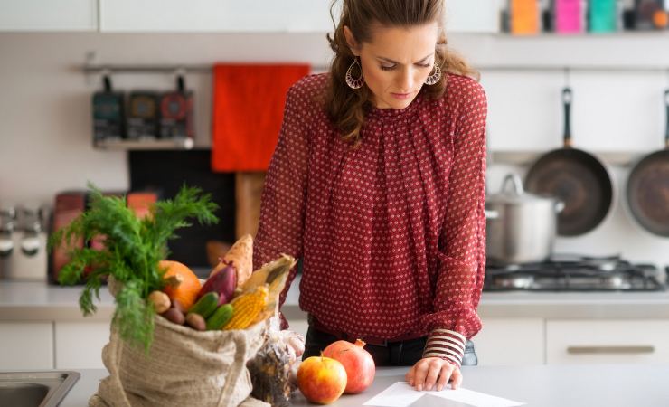 Donna in cucina che guarda lista spesa con sacchetto frutta e verdura accanto