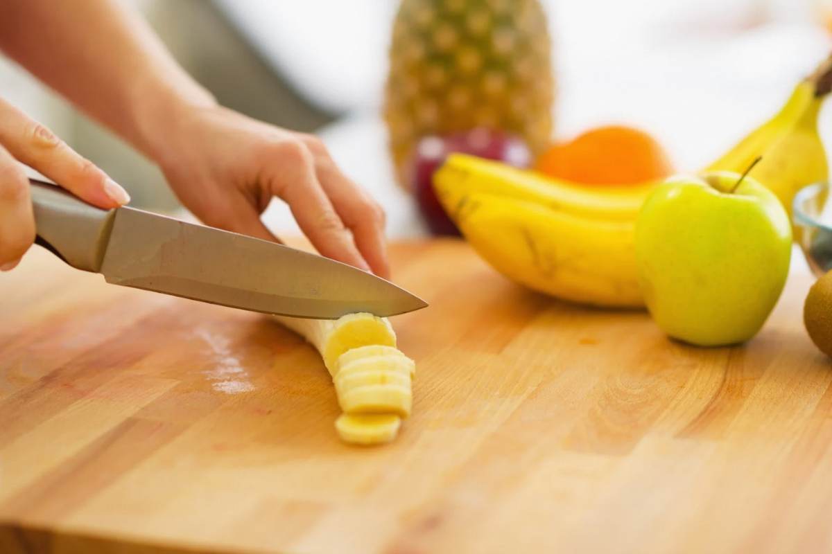 Donna che taglia una banana su un tagliere con frutta