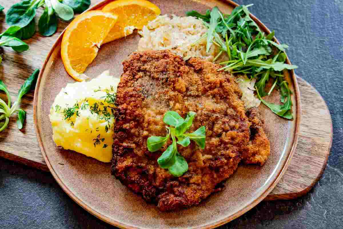una cotoletta in un piatto con fettine di arancia, verdura e purè