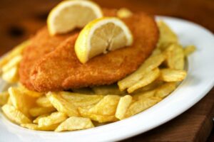 cotolette impanate su un piatto con sopra delle fettine di limone sopra un letto di patatine fritte