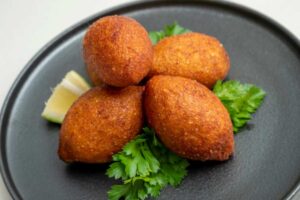 crocchette fritte su un piatto sopra ad un letto d'insalata con accanto una fetta di limone